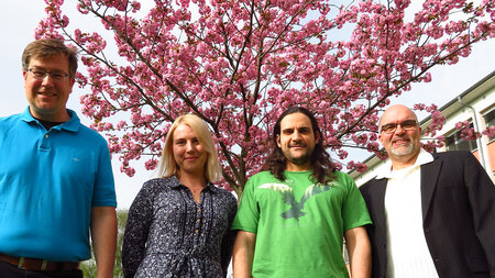 Three men and a woman stand in front of a blossoming tree